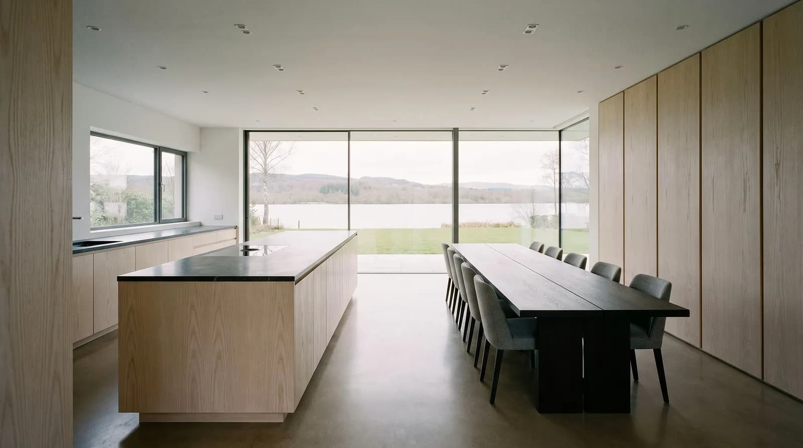 Esempio di cucina: lunga isola con frontali in legno e tavolo da pranzo davanti a una vetrata con vista lago.
